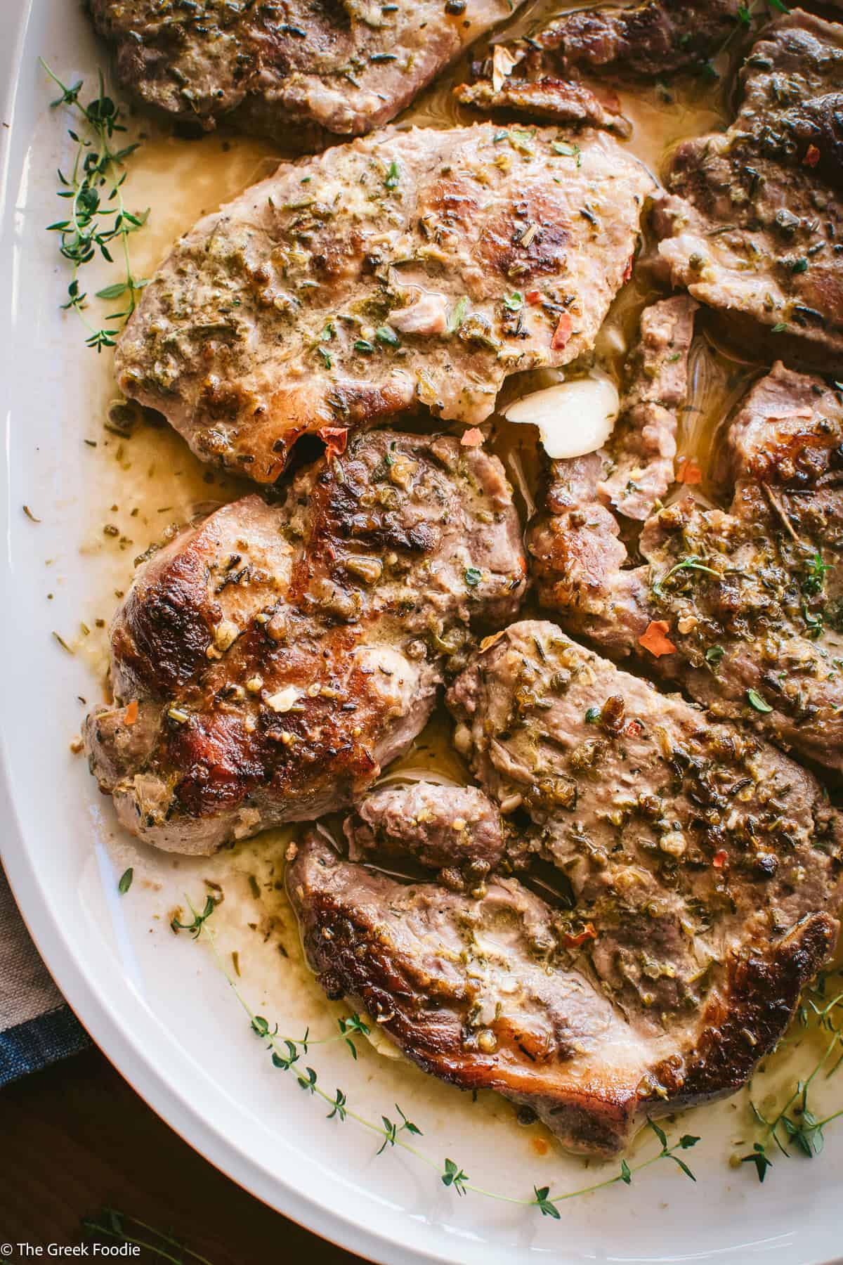 Boneless Greek pork steaks on a serving platter with lemon oregano pan sauce and fresh herbs