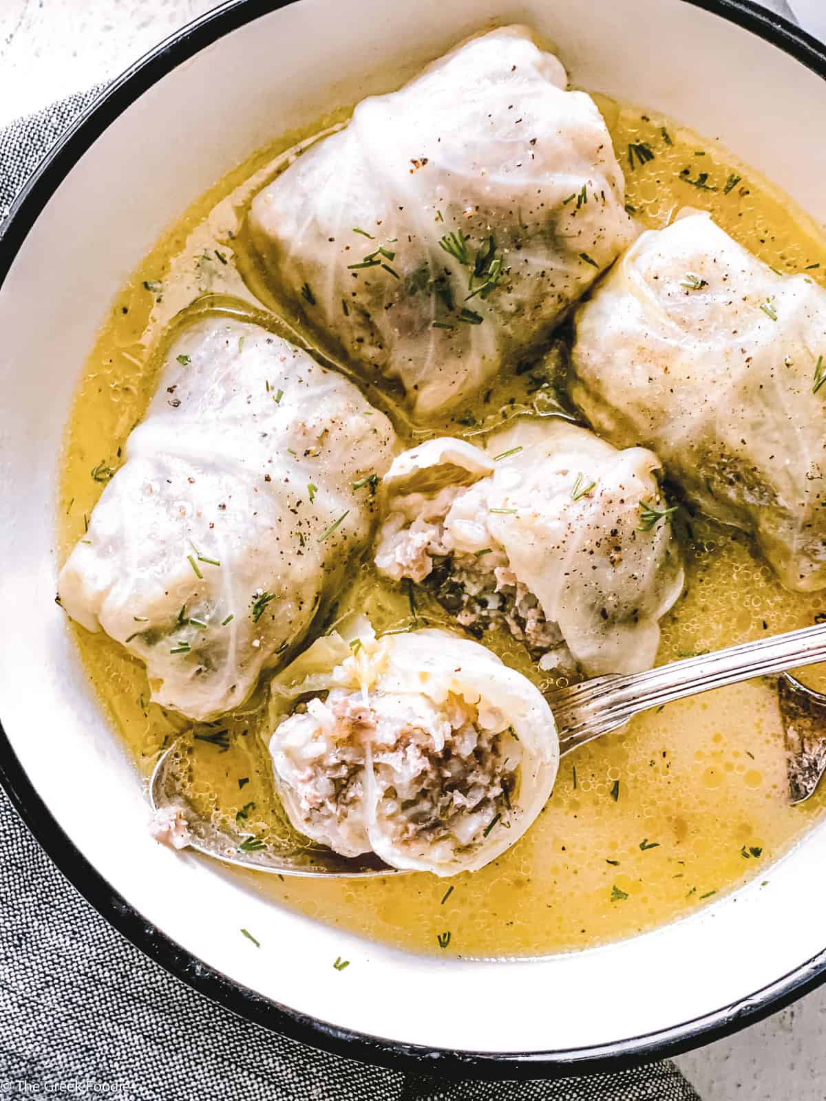 Close-up of a lahanodolmades roll opened to reveal the rice and meat filling in egg-lemon sauce