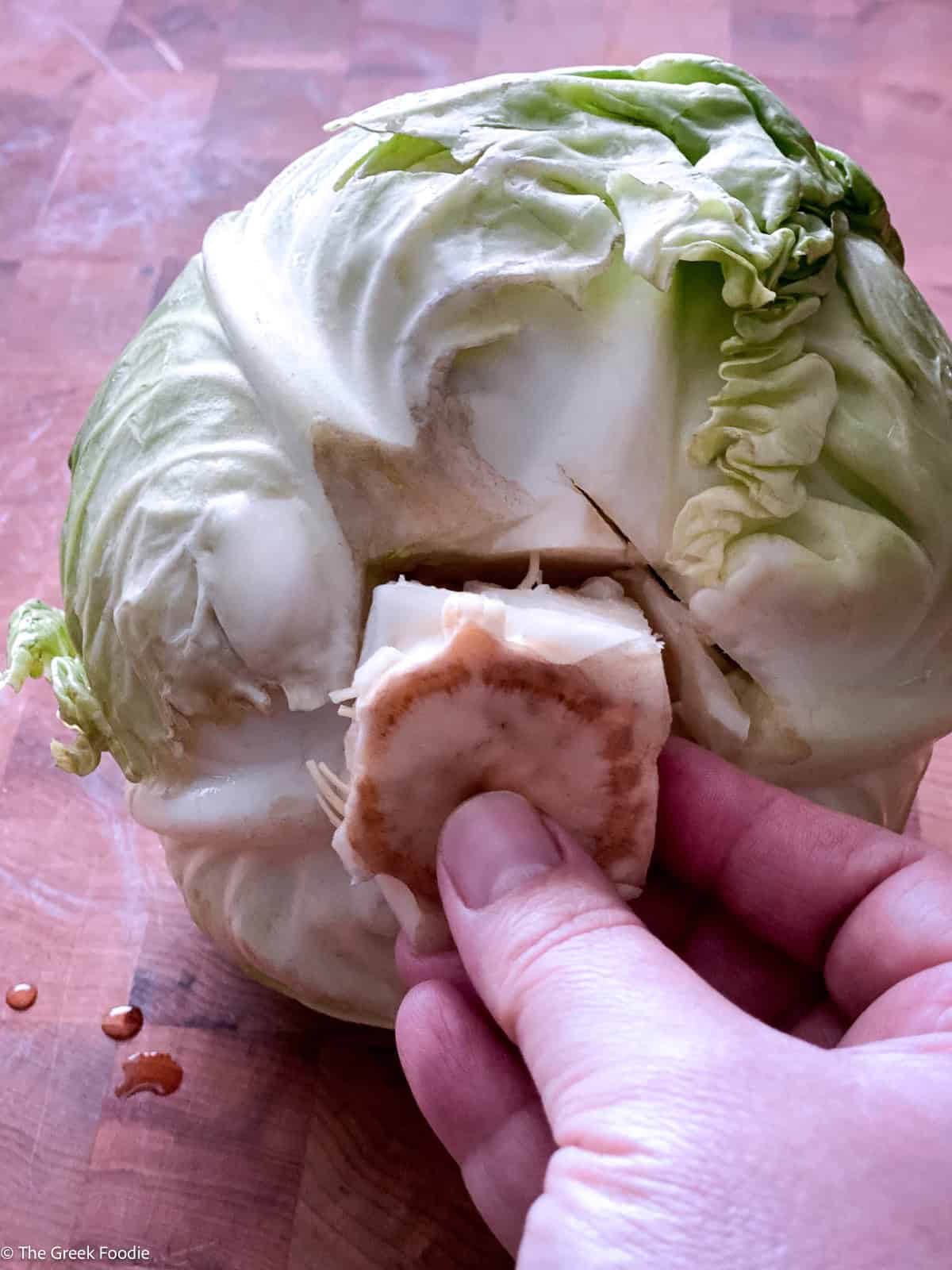 Hand pulling the cut core out of a whole green cabbage on a wooden board