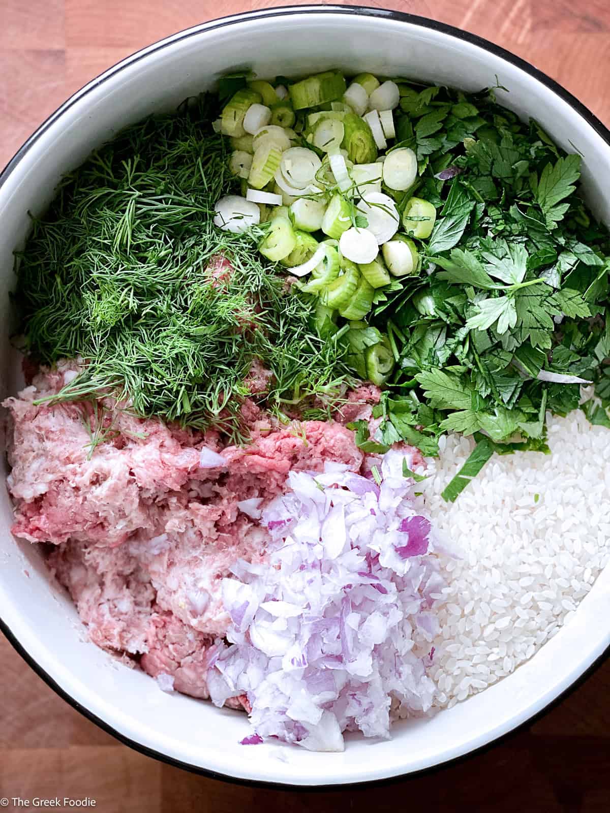 Bowl of lahanodolmades filling with ground meat, rice, diced red onion, dill, parsley and scallions before mixing