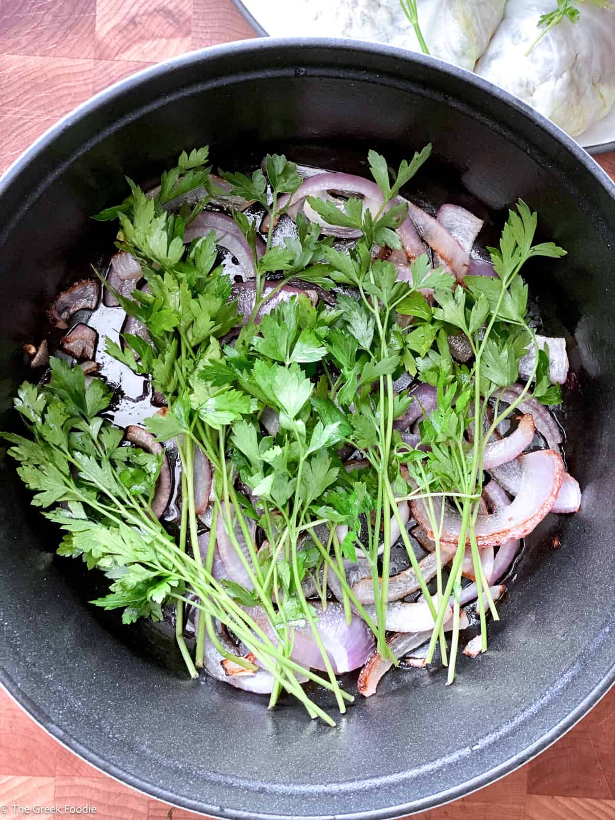 Sliced red onion and whole parsley sprigs lining the base of a black pot