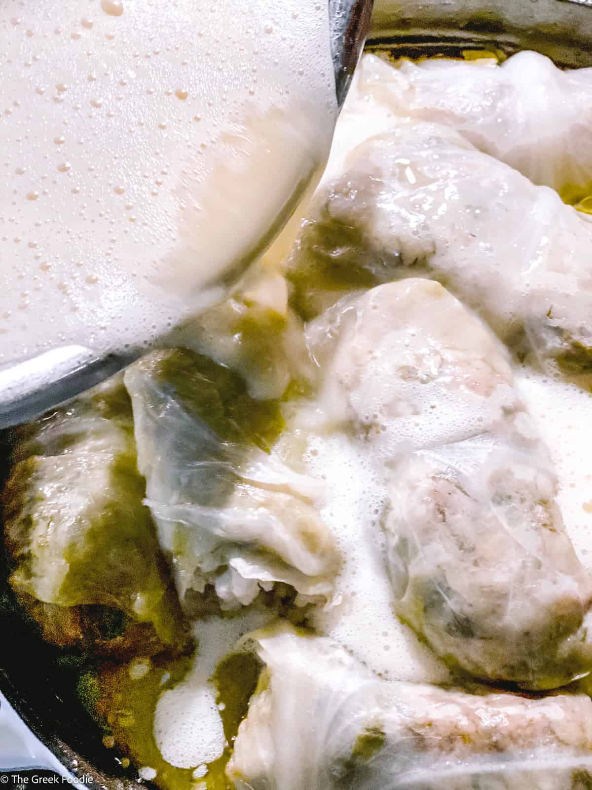 Avgolemono sauce poured over the cabbage rolls in the pot