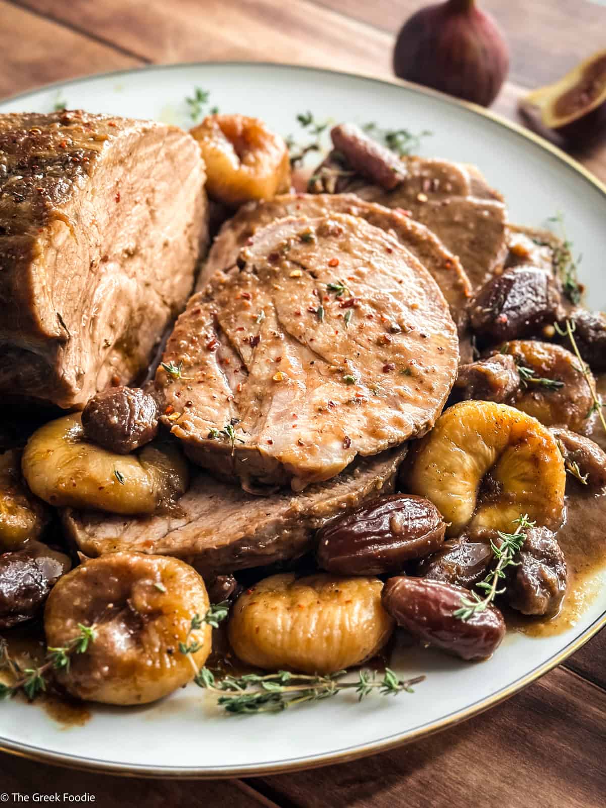Pork pot roast platter surrounded by braised figs, dates, chestnuts and sprigs of fresh thyme