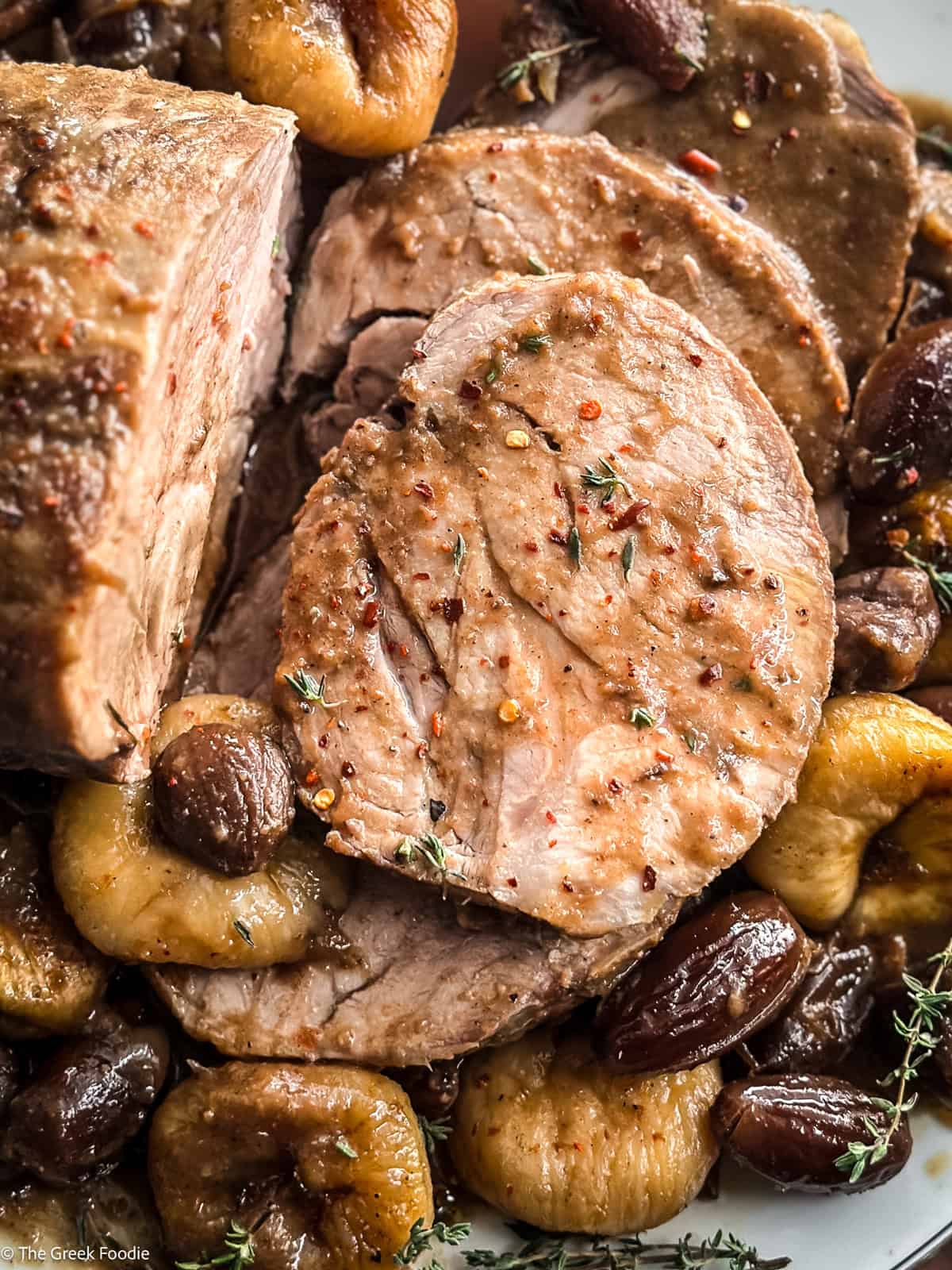 Close-up of a tender slice of pork pot roast topped with thyme and cracked pepper, figs and dates beneath