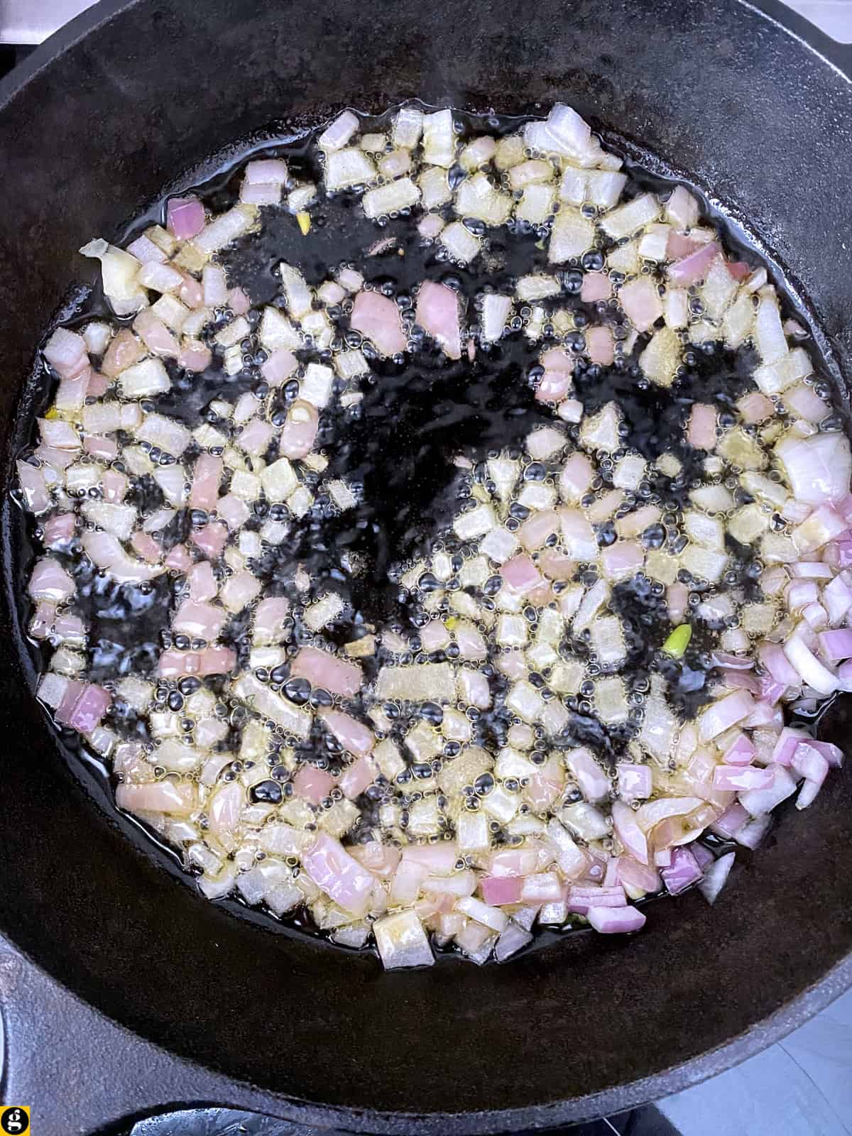 Diced red onion sizzling in olive oil in a cast iron skillet.