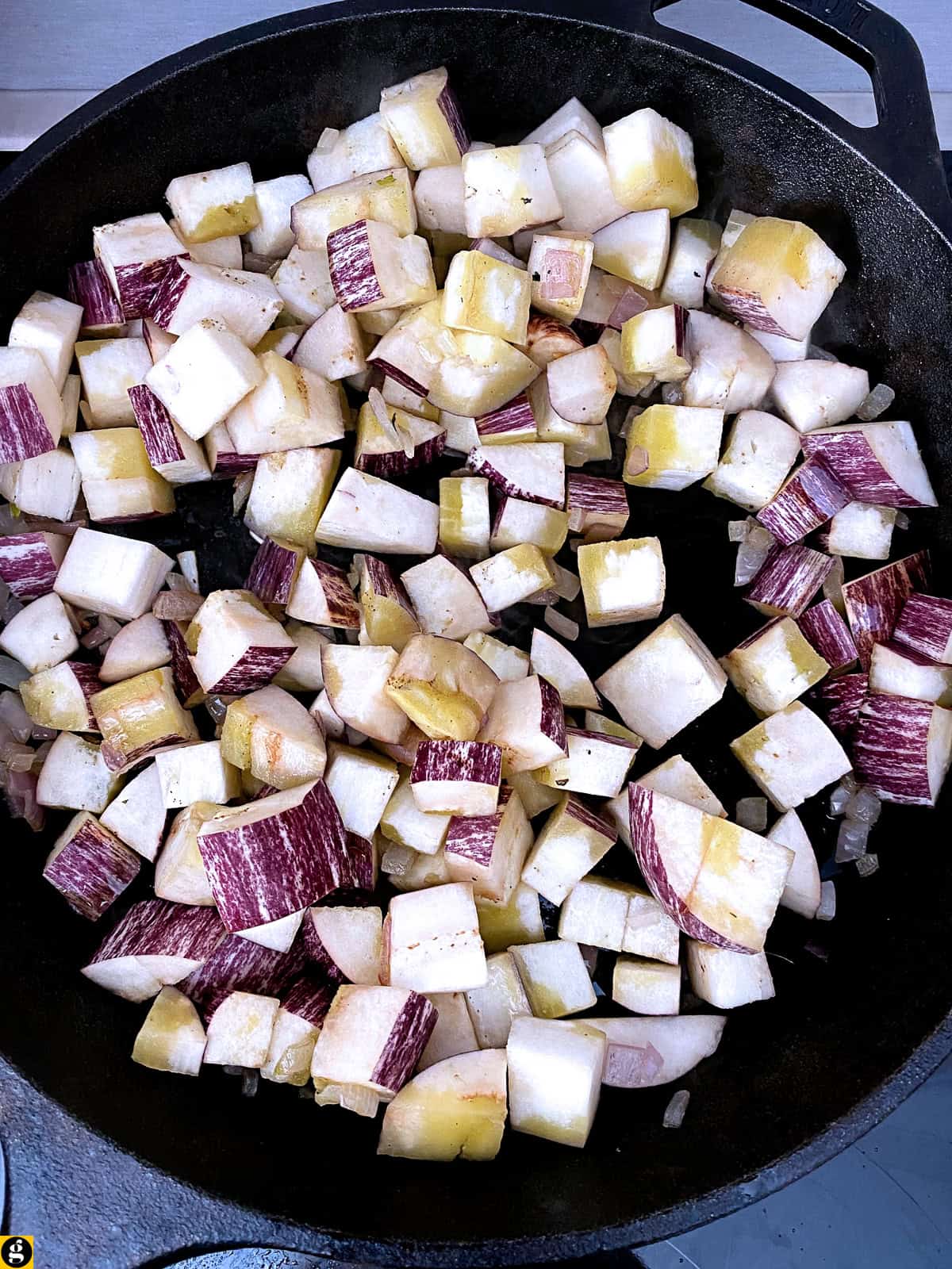 Diced eggplant added to the onion in a cast iron skillet.