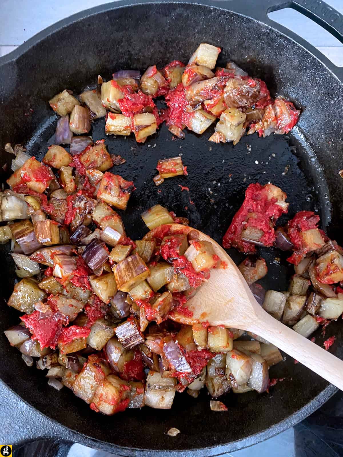 Browned eggplant stirred with tomato paste in a cast iron skillet.
