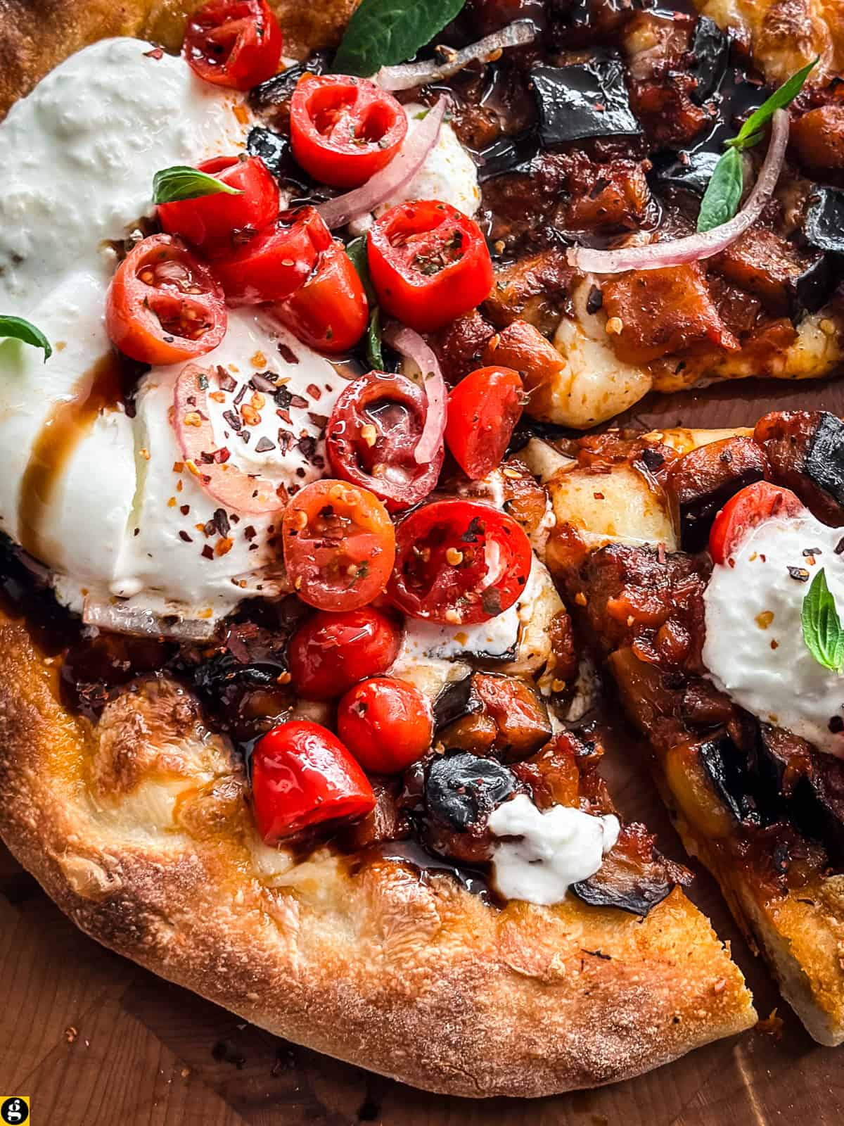 Close-up of a slice of burrata pizza with eggplant, cherry tomatoes, and a spoonful of creamy burrata.