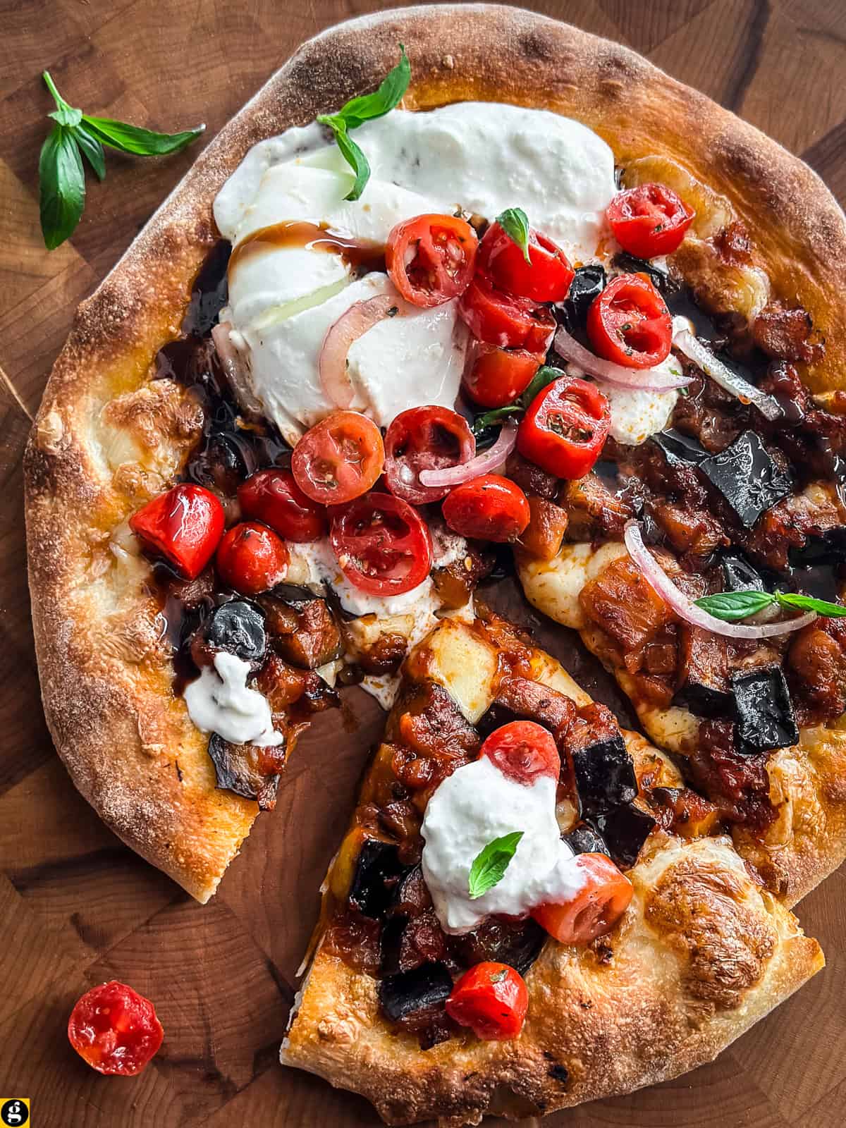 Burrata pizza with eggplant and cherry tomato salad on a wooden board, with one slice pulled away.