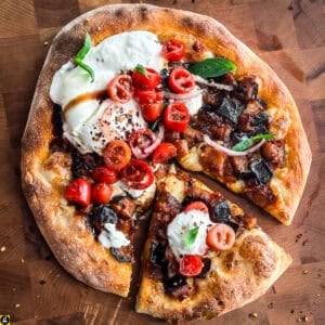 Overhead view of a sliced burrata pizza with eggplant, topped with torn burrata, cherry tomatoes, red onion, basil, chili flakes, and balsamic glaze.