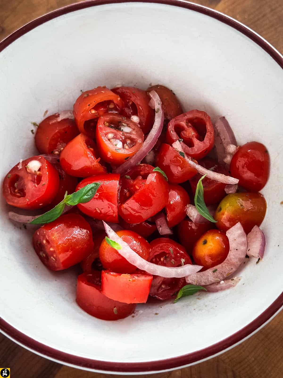 Cherry tomato salad with sliced red onion, basil, and oregano in a white bowl.