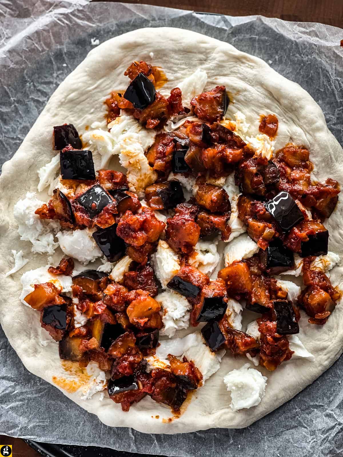 Pizza dough on parchment topped with torn fresh mozzarella and Greek-style eggplant, ready for the oven.
