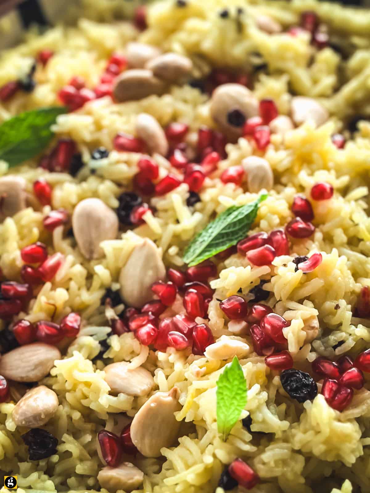 Close-up of saffron rice pilaf showing separate golden grains with toasted almonds, Corinthian currants and pomegranate seeds.