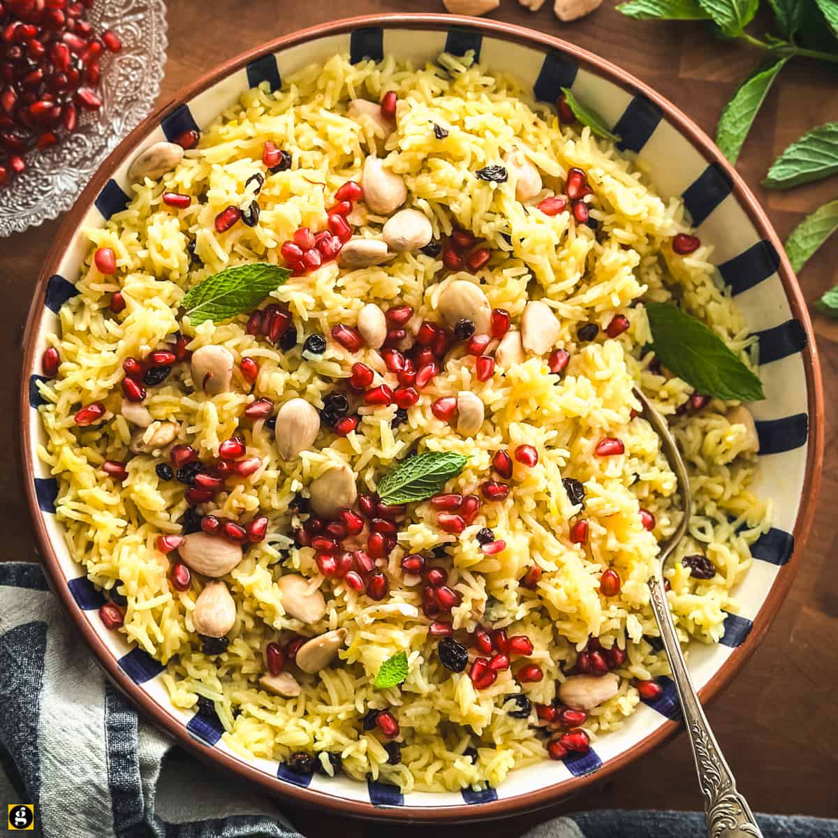 Overhead view of Greek saffron rice pilafi in a blue and white striped bowl with a serving spoon.