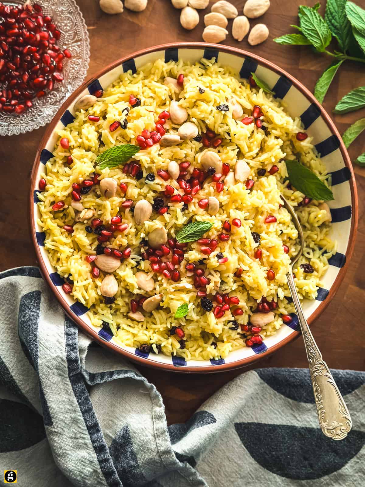 Greek saffron rice pilaf with almonds, currants and pomegranate, served in a striped bowl on a wooden table.