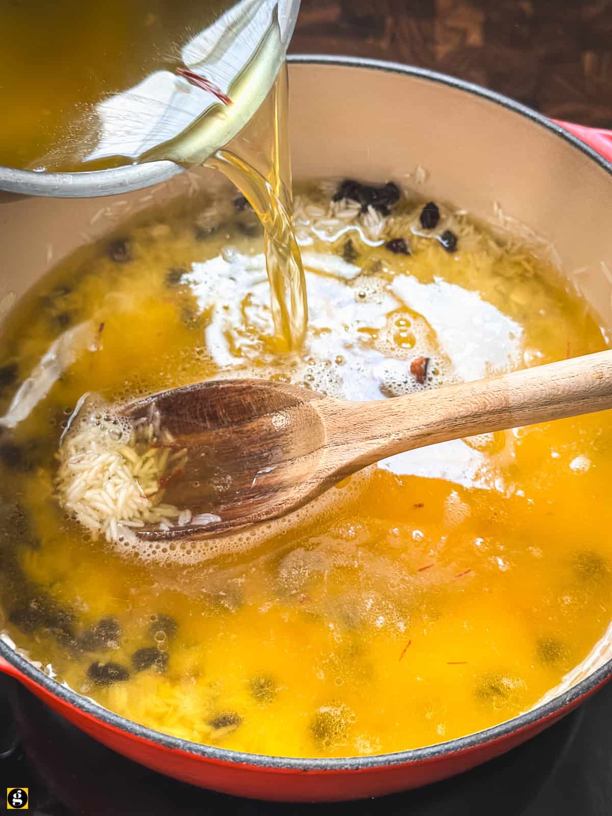 Hot saffron chicken stock poured over rice and currants in a red Dutch oven.