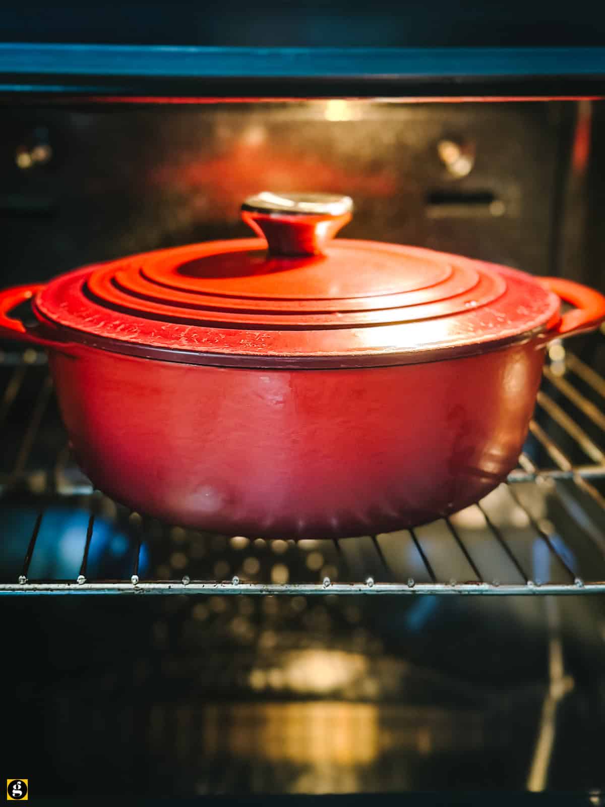 Covered red Dutch oven baking Greek saffron rice pilaf on an oven rack.