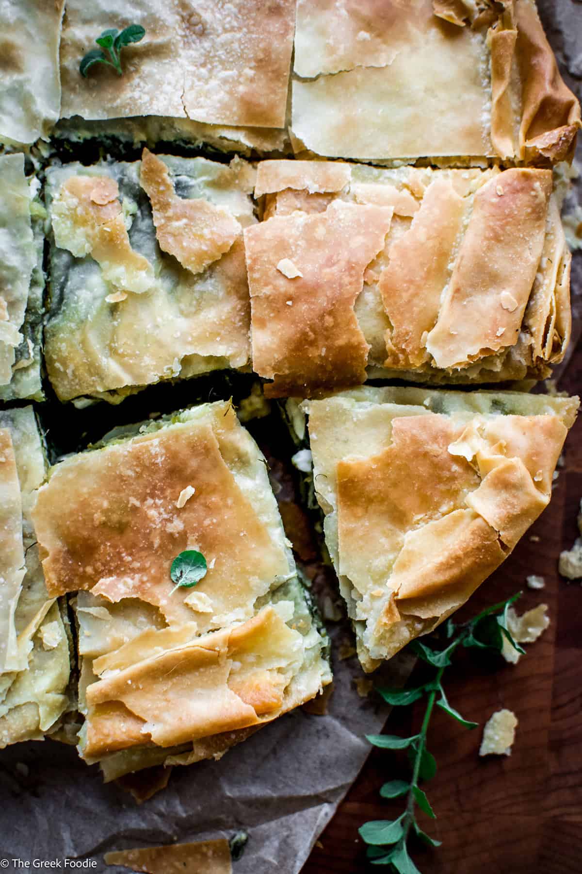 Pieces of Greek spinach pie on parchment paper, topped with fresh oregano leaves.