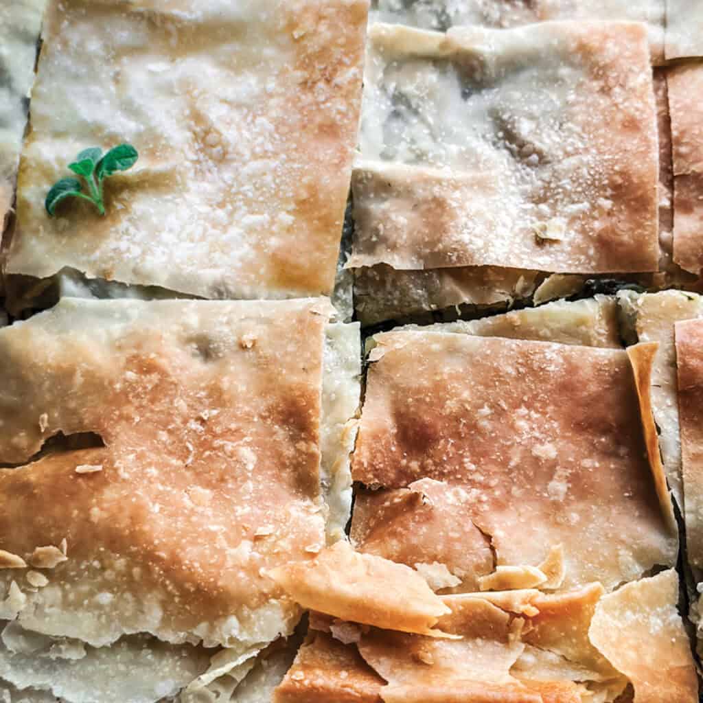 Greek spinach pie topped with fresh oregano leaves.