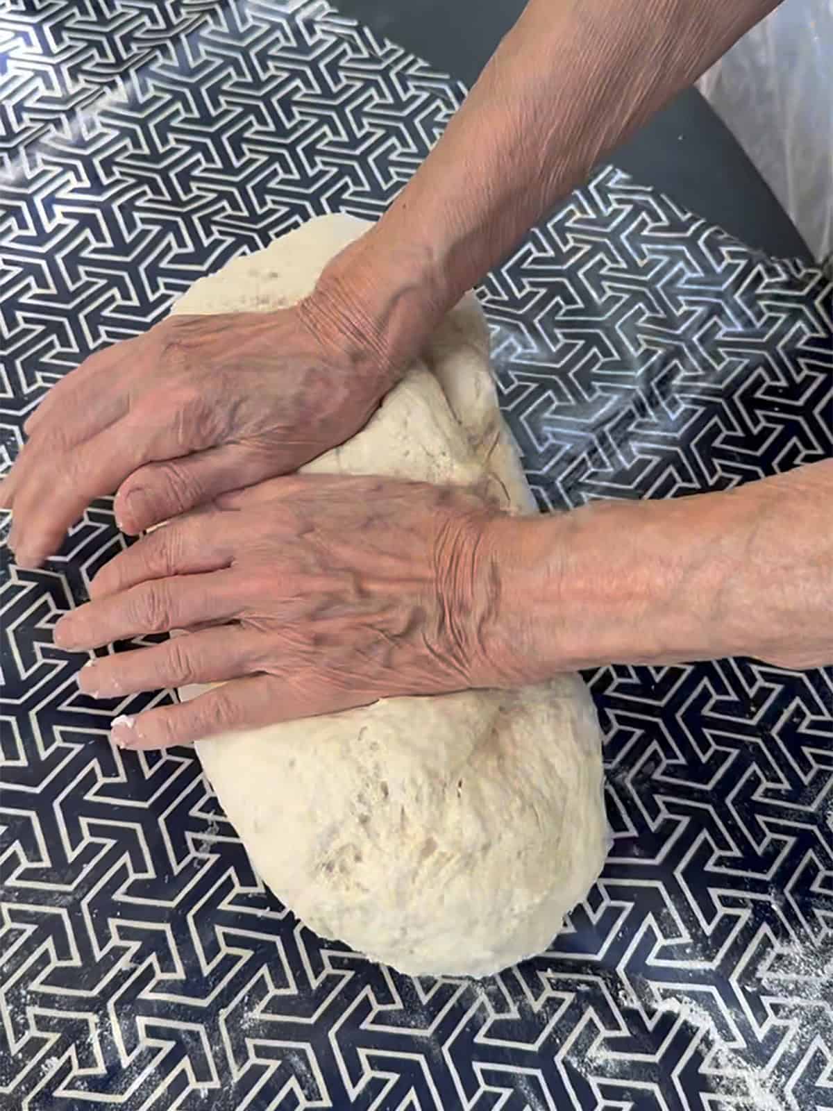 Hands kneading homemade phyllo dough on a floured table.