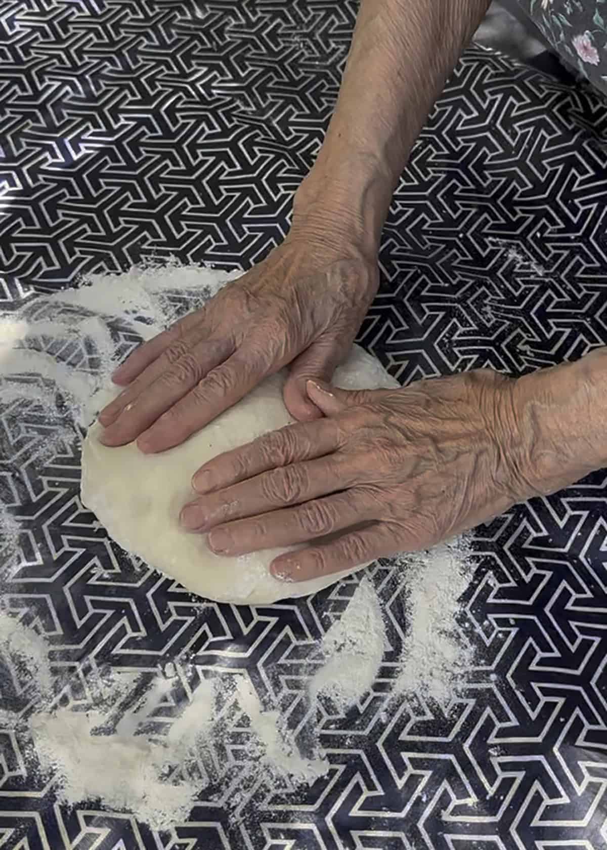 A ball of phyllo dough pressed flat with the palms on a floured surface.