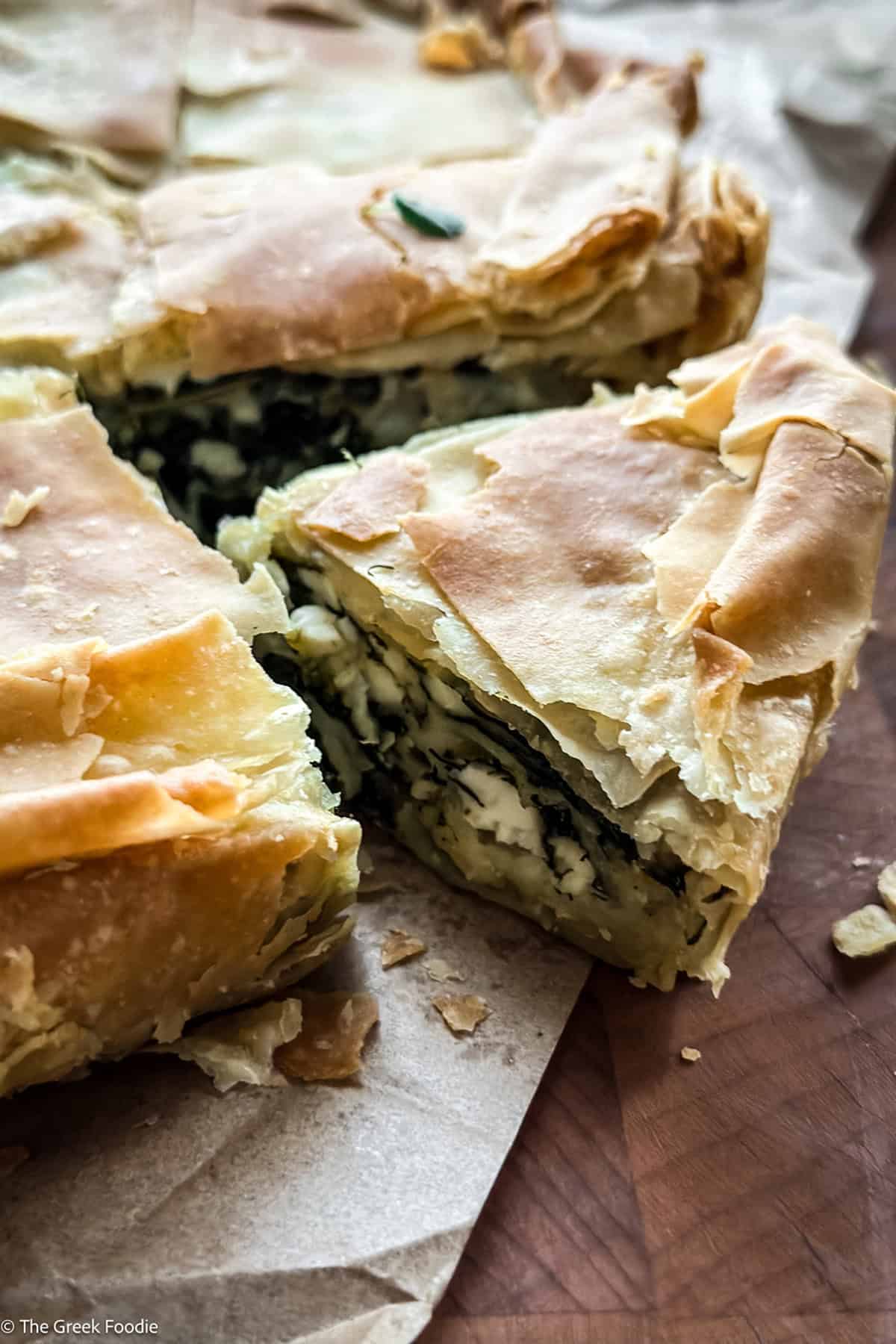 A wedge of spanakopita lifted from the pie, showing spinach and feta filling between layers of crisp phyllo.