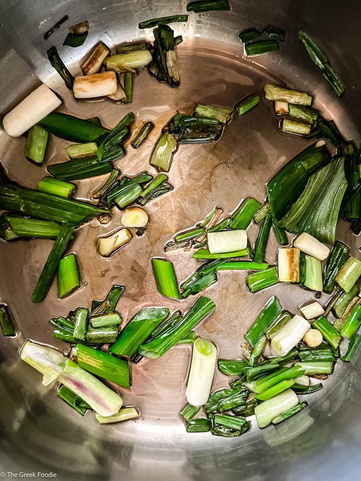 Chopped spring onions softening in olive oil in a skillet.