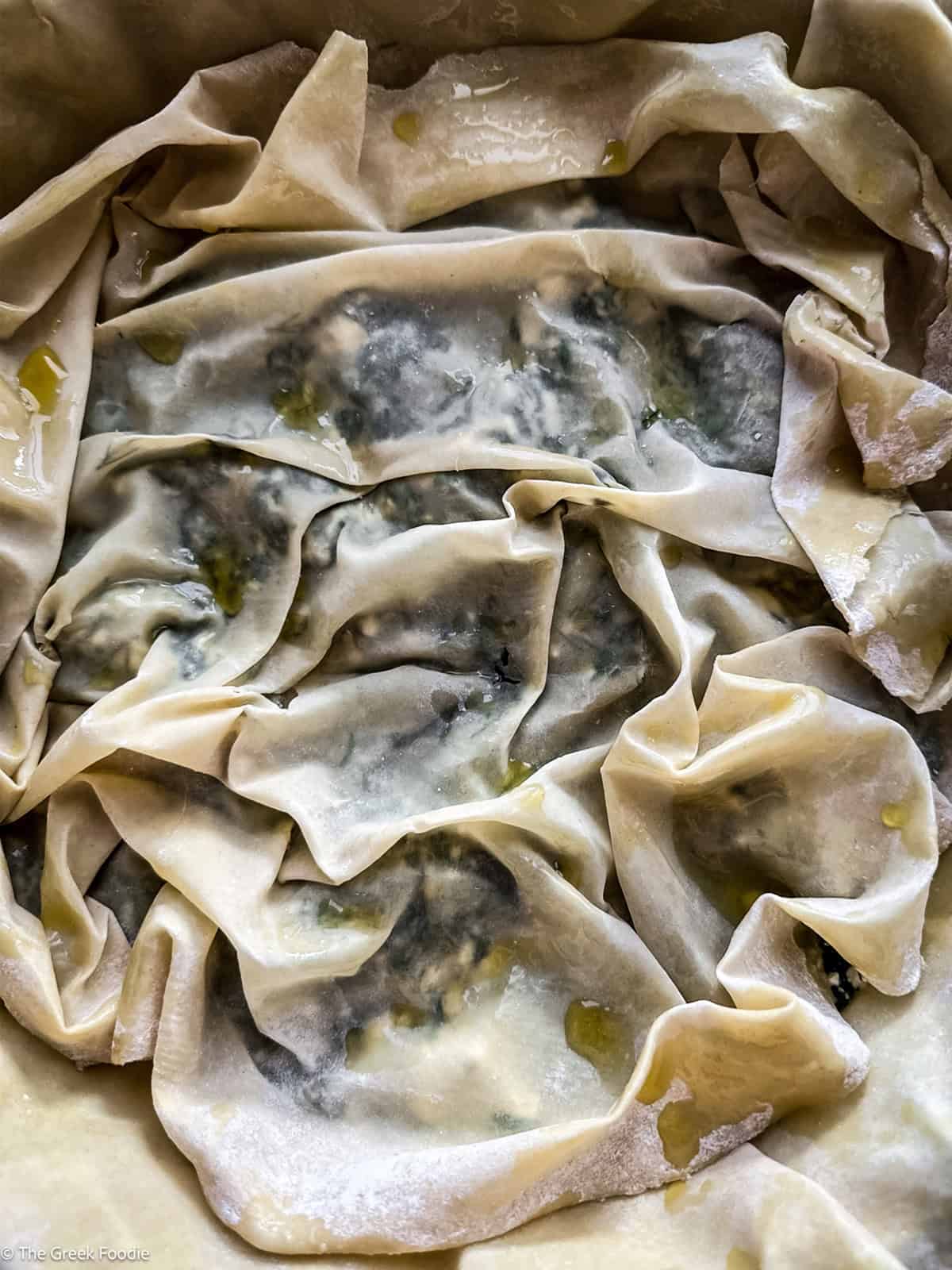 A wrinkled phyllo sheet layered over the spanakopita filling.