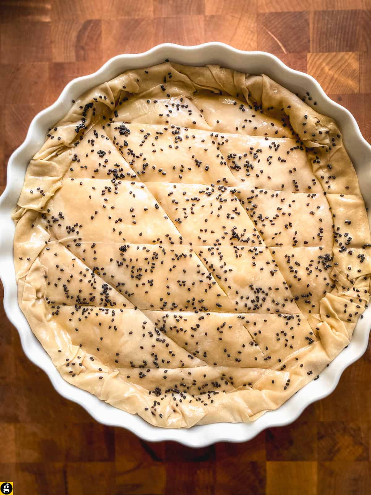 Unbaked phyllo pie scored and sprinkled with black sesame, ready for the oven
