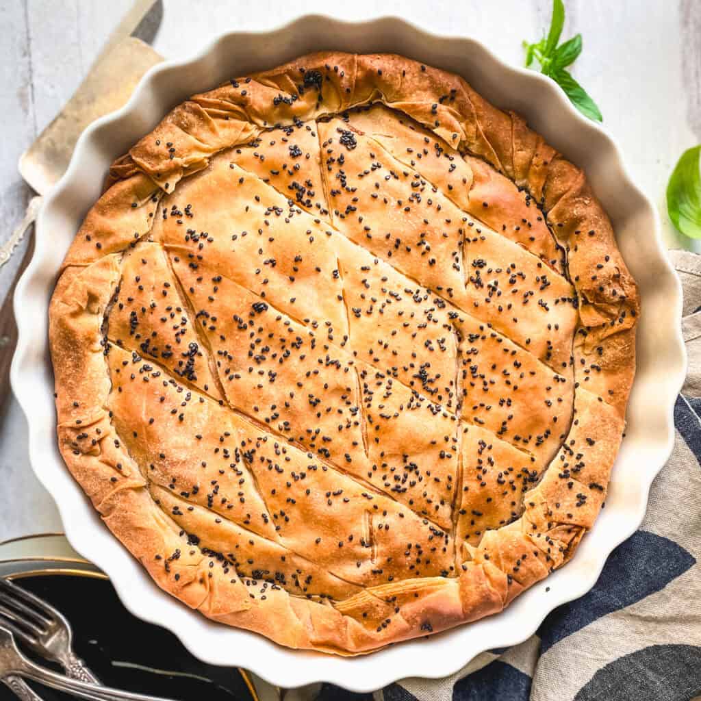 Golden kasseri cheese pie with pastirma, topped with black sesame, in a white fluted tart pan