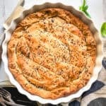 Golden kasseri cheese pie with pastirma, topped with black sesame, in a white fluted tart pan