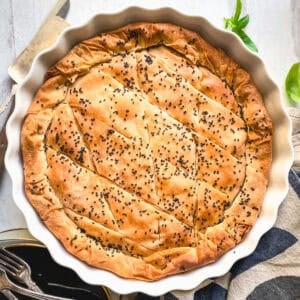 Golden kasseri cheese pie with pastirma, topped with black sesame, in a white fluted tart pan