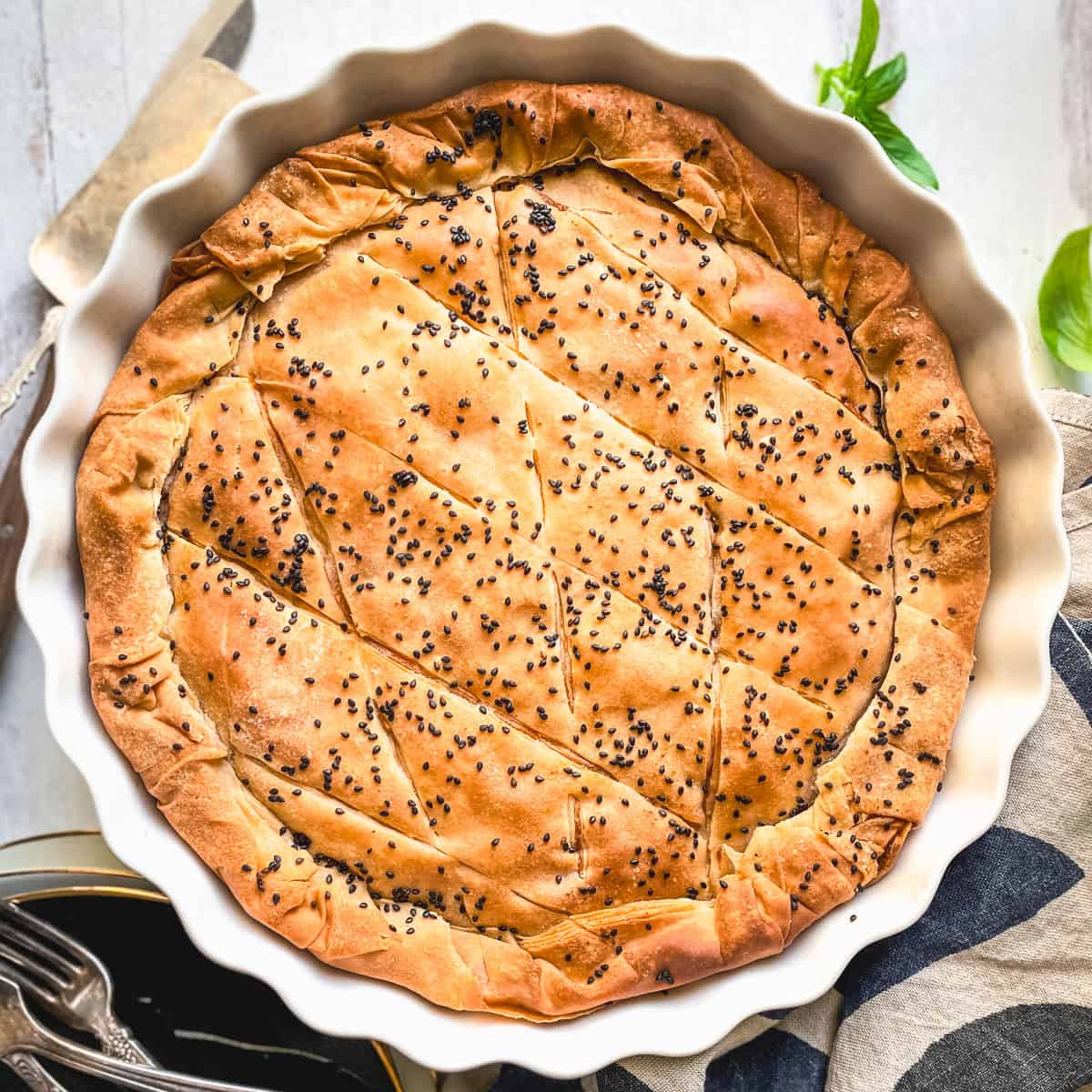 Golden kasseri cheese pie with pastirma, topped with black sesame, in a white fluted tart pan