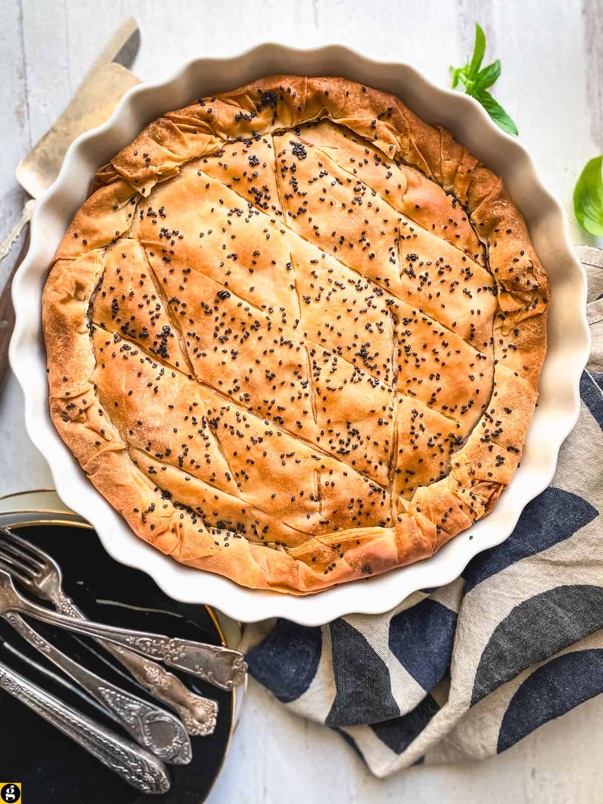 Golden kasseri cheese pie with pastirma, topped with black sesame, in a white fluted tart pan, on a table ready for serving