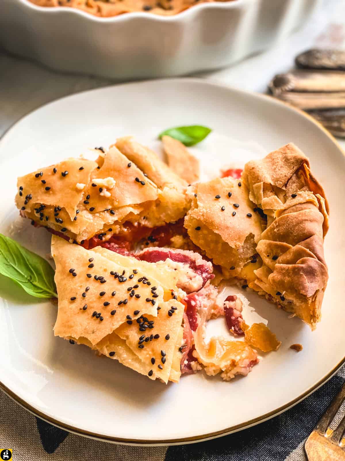 Slices of kasseri cheese pie on a white plate, showing pastirma and tomato inside the phyllo